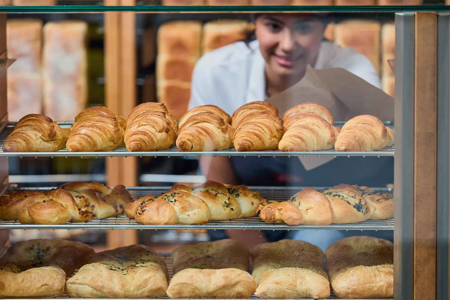 The sales associate meticulously retrieves a freshly baked croissant for a hungry customer.