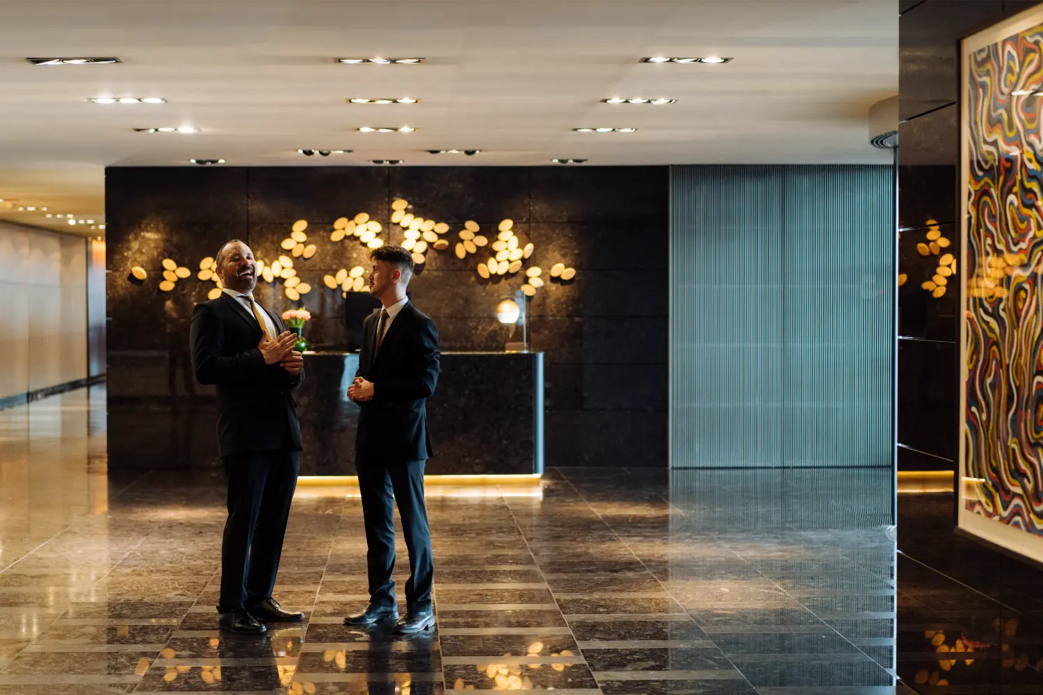 Two hotel colleagues sharing a laugh in the lobby - a moment of connection and care that brings comfort and positivity.