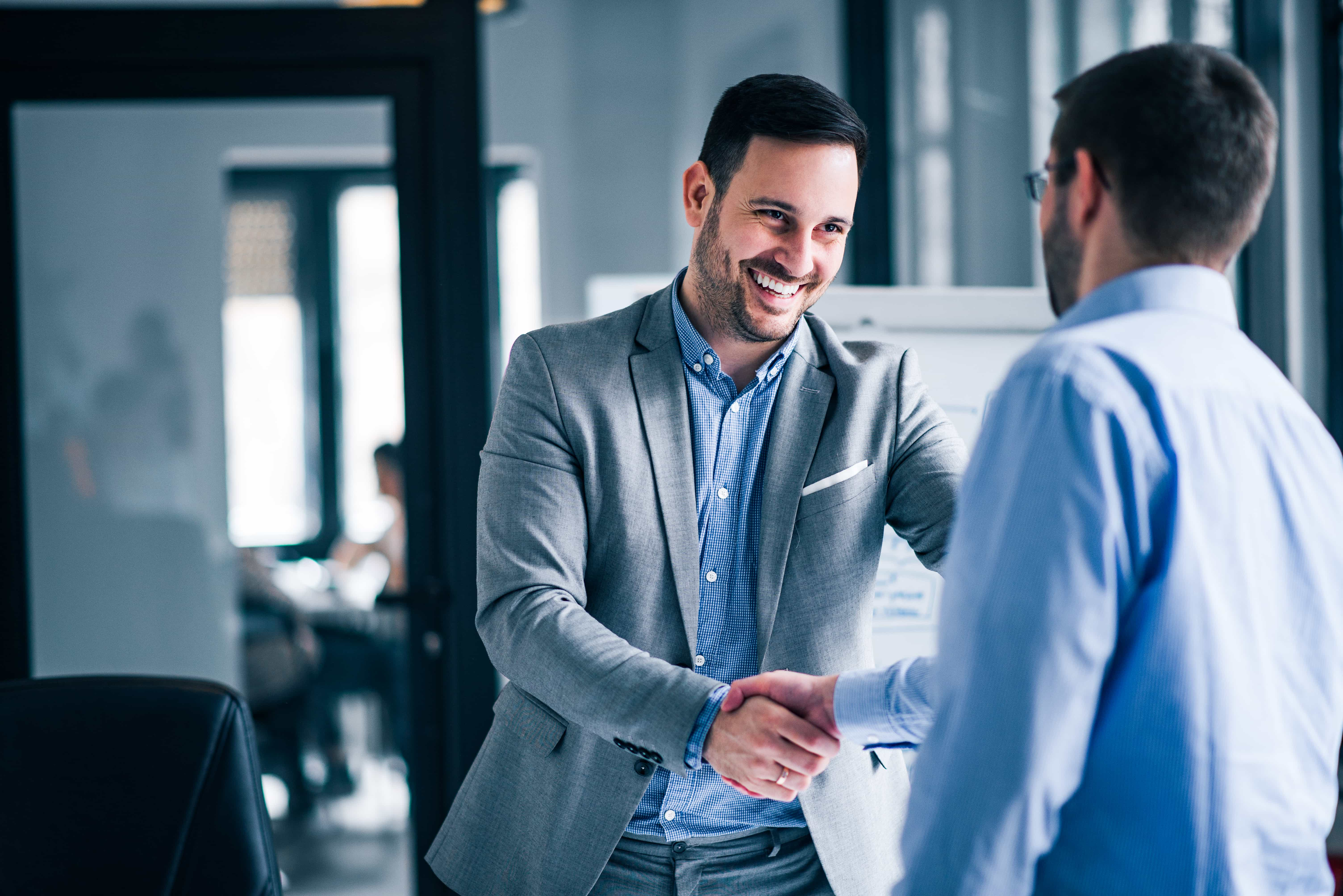 two smiling businessmen shaking hands while standing office 1